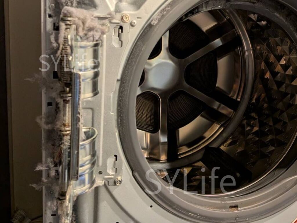 東京都葛飾区のNA-LX129CL分解時の前面内部。ドアヒンジ周辺や鉄板部分にホコリが付着している状態。